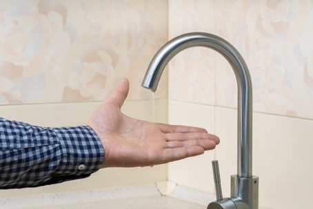 Close up of man's hand testing low water pressure at kitchen tap.