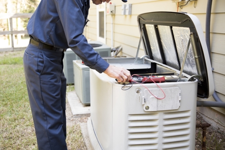 Electrician inspecting a home standby generator during maintenance outside a house.