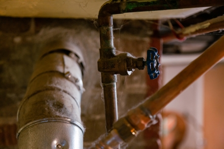 Old, dusty water pipe with a blue shutoff valve in a basement.